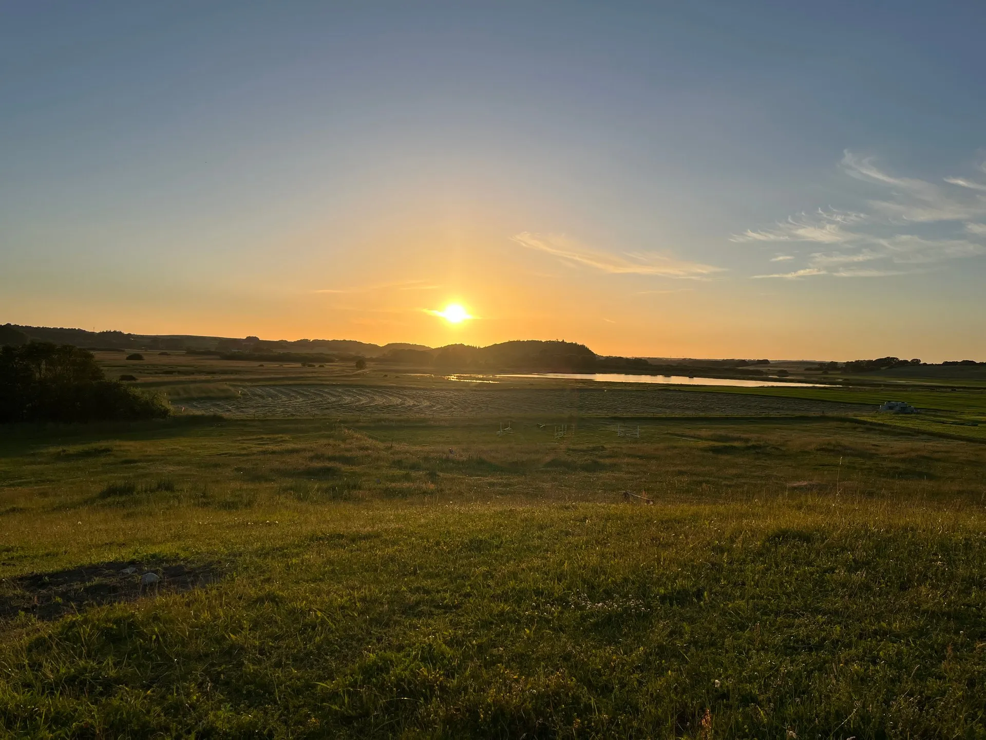 Solnedgang over ådalen med eng, høslæt og søen i baggrunden